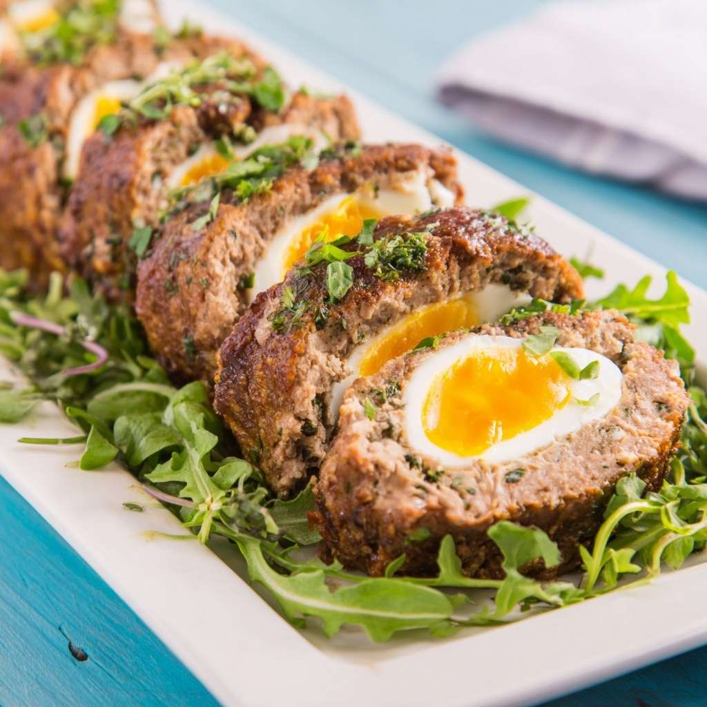 Pain de kefta marocain aux œufs, tranché et servi chaud, viande épicée fondante avec œufs au centre sur lit de verdure.