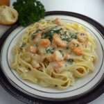 Tagliatelles aux fruits de mer nappées de sauce crémeuse, crevettes et persil frais, servies bien chaudes dans une assiette généreuse.