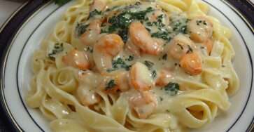 Tagliatelles aux fruits de mer nappées de sauce crémeuse, crevettes et persil frais, servies bien chaudes dans une assiette généreuse.