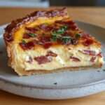 Quiche aux lardons et fromage dorée au four, texture fondante à l’intérieur, servie en parts avec herbes fraîches.