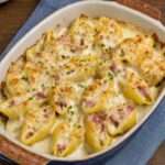 Conchiglioni farcis au jambon nappés de béchamel onctueuse et fromage gratiné, servis bien chauds dans un plat à gratin doré.
