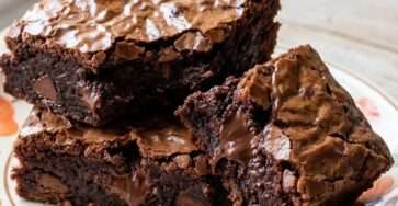 Carrés de brownies fondants aux morceaux de chocolat noir et pépites visibles, texture dense et humide au centre, posés sur une grille avec papier cuisson.