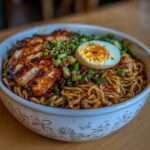 Bol de ramen au chashu avec bouillon shoyu foncé, nouilles ramen fraîches, tranches de poitrine de porc braisée caramélisée, œuf mollet coupé en deux, oignons verts et graines de sésame.