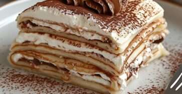 Tiramisu aux crêpes roulées imbibées de café, garnies de crème mascarpone et saupoudrées de cacao amer, présenté en plat rectangulaire avec couches visibles.