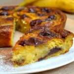 Clafoutis banane chocolat maison dans un moule beurré, bananes en rondelles et morceaux de chocolat noir fondants, surface dorée et légèrement gonflée à la sortie du four.