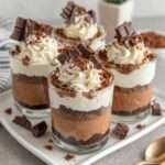 Verrines en verre garnies de mousse au chocolat noir onctueuse, couche de biscuits chocolat émiettés, chantilly vanillée pochée en spirale et saupoudrée de cacao.