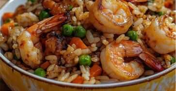 Wok de riz sauté aux crevettes roses, petits pois verts, dés de carotte, œufs brouillés et sauce soja brillante, servi chaud avec oignon nouveau émincé.