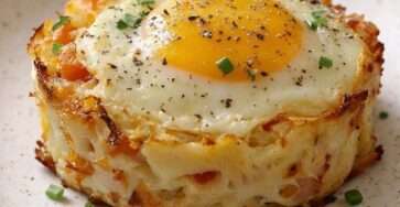 Gratin de pâtes crémeuses légèrement dorées sur les bords, avec un œuf au jaune coulant au centre, parsemé de ciboulette fraîche dans un ramequin en céramique.