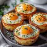 Muffins de pommes de terre dorés et croustillants formant des nids, garnis d’un œuf au jaune coulant au centre, parsemés de persil frais dans un moule à muffins.