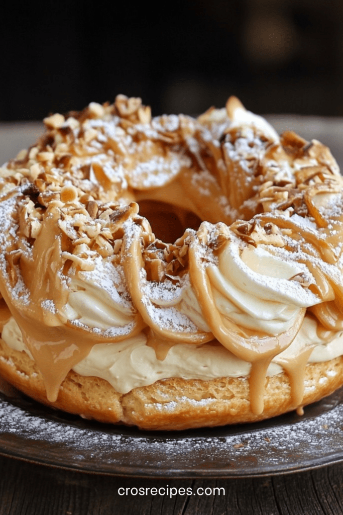 Paris-Brest traditionnel en couronne de pâte à choux dorée, garni d’une crème pralinée onctueuse et décoré d’amandes effilées et de sucre glace.