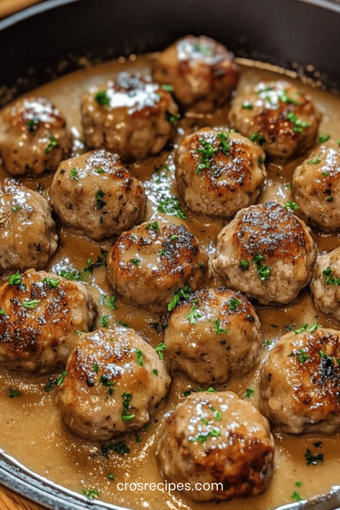 Boulettes de viande dorées mijotées dans une sauce brune onctueuse avec persil frais, servies dans une poêle rustique.