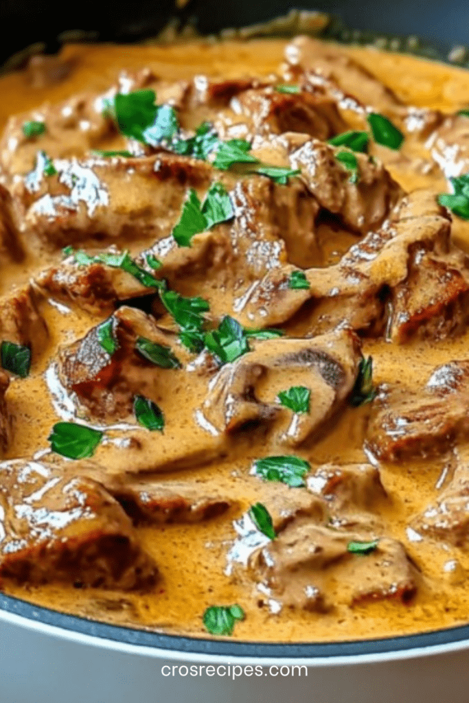 Bœuf Stroganoff crémeux aux champignons servi dans une assiette avec sauce onctueuse, persil frais et accompagnement de pâtes.