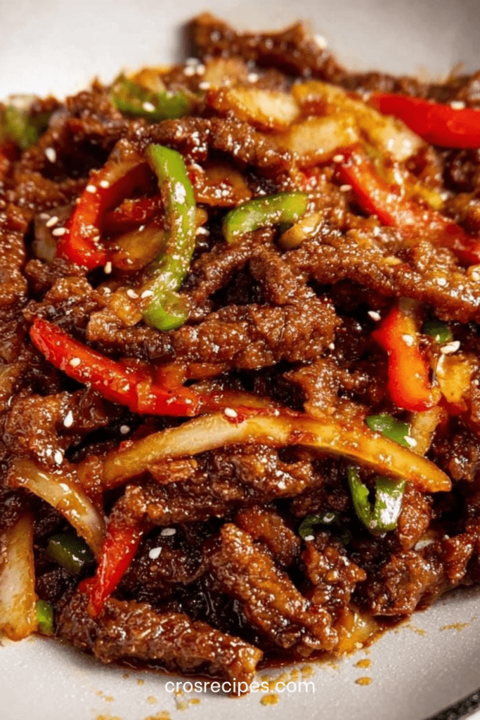 Lamelles de bœuf croustillantes enrobées d’une sauce brillante sucrée épicée, accompagnées de poivrons rouges et verts et d’oignons dans un wok.