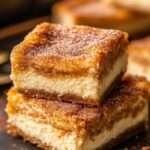Carrés cheesecake churros dorés avec cœur crémeux au fromage frais et finition sucre-cannelle, servis sur une assiette.