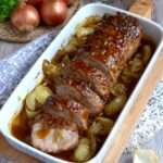 Rôti de porc au miel et aux oignons fondants servi en tranches avec sauce brillante, oignons caramélisés et herbes, présenté dans un plat rustique.