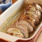 Tranches de rôti de porc nappées de sauce moutarde crémeuse dans une cocotte avec oignons fondants et herbes, servies avec pommes de terre.