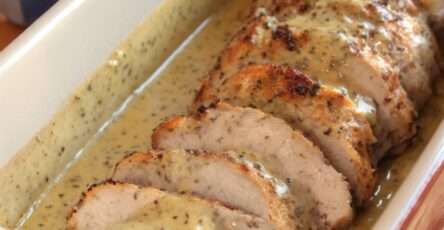 Tranches de rôti de porc nappées de sauce moutarde crémeuse dans une cocotte avec oignons fondants et herbes, servies avec pommes de terre.