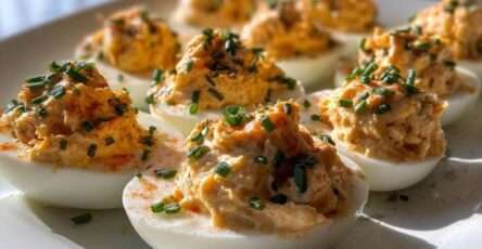 Œufs mimosa garnis de poulet Buffalo crémeux, décorés de paprika et de ciboulette fraîche, servis sur un plateau pour un apéritif.