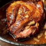 Rouelle de porc confite servie dans une cocotte avec une sauce brune aux oignons caramélisés et à l’ail, viande fondante nappée généreusement, plat rustique et familial.