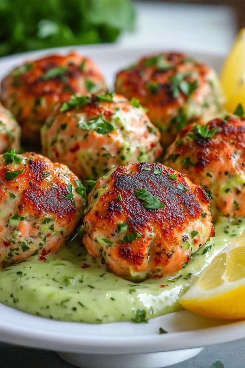 Boulettes de saumon dorées au four servies avec une crème d’avocat onctueuse et citronnée, décorées de persil frais sur une assiette claire.