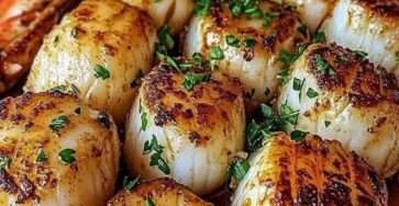 Noix de Saint-Jacques dorées à la poêle nappées de beurre citronné avec persil frais et quartiers de citron dans une assiette élégante.