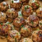 Boulettes de viande dorées mijotées dans une sauce brune onctueuse avec persil frais, servies dans une poêle rustique.