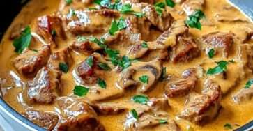 Bœuf Stroganoff crémeux aux champignons servi dans une assiette avec sauce onctueuse, persil frais et accompagnement de pâtes.
