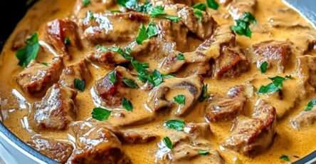 Bœuf Stroganoff crémeux aux champignons servi dans une assiette avec sauce onctueuse, persil frais et accompagnement de pâtes.