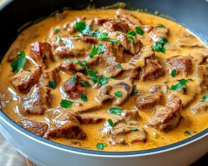 Bœuf Stroganoff crémeux aux champignons servi dans une assiette avec sauce onctueuse, persil frais et accompagnement de pâtes.