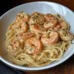 Spaghettis crémeux aux crevettes, ail et parmesan servis dans une assiette avec persil frais et sauce onctueuse.