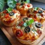 Mini pizzas maison garnies de mozzarella fondante, tomates cerises coupées en deux, olives noires, basilic frais et herbes, servies chaudes sur une assiette.`