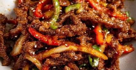 Lamelles de bœuf croustillantes enrobées d’une sauce brillante sucrée épicée, accompagnées de poivrons rouges et verts et d’oignons dans un wok.
