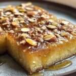 Gâteau moelleux aux amandes imbibé de miel, doré et décoré d’amandes croquantes sur le dessus, servi en part sur une assiette