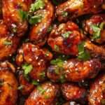 Ailes de poulet caramélisées nappées de sauce sucrée épicée, brillantes, garnies de sésame et herbes fraîches dans une assiette