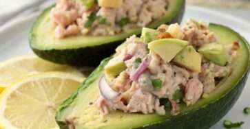 Avocats farcis au thon crémeux avec yaourt grec, citron et cornichons, servis frais avec une texture onctueuse et une présentation élégante.