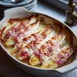 Roulés d’endives au jambon nappés de sauce béchamel et gratinés au four, servis dans un plat doré avec fromage fondu et surface légèrement croustillante.