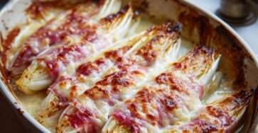 Roulés d’endives au jambon nappés de sauce béchamel et gratinés au four, servis dans un plat doré avec fromage fondu et surface légèrement croustillante.