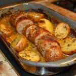 Andouillettes rôties au four accompagnées de pommes de terre dorées aux herbes et à l’ail, servies dans un plat rustique avec jus de cuisson.