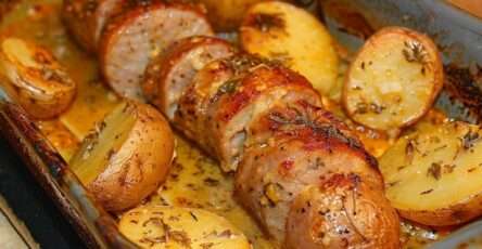 Andouillettes rôties au four accompagnées de pommes de terre dorées aux herbes et à l’ail, servies dans un plat rustique avec jus de cuisson.