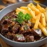Assiette de carbonade flamande traditionnelle avec morceaux de bœuf fondants dans une sauce brune à la bière, servie avec des frites croustillantes.
