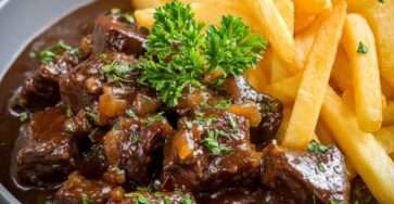 Assiette de carbonade flamande traditionnelle avec morceaux de bœuf fondants dans une sauce brune à la bière, servie avec des frites croustillantes.
