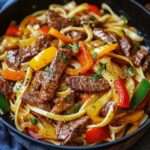 Assiette de nouilles sautées au bœuf avec poivrons rouges, jaunes et verts, oignon émincé et herbes fraîches, servie bien chaude dans un style asiatique gourmand.