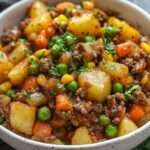 Hachis de bœuf aux légumes servi chaud, avec pommes de terre fondantes, carottes, petits pois et persil frais dans une poêle rustique.