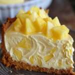 Cheesecake ananas sans cuisson, décoré de morceaux d’ananas juteux sur une crème blanche ultra crémeuse et une base biscuitée dorée.