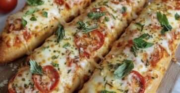 Baguette gratinée façon pizza sortie du four, garnie de sauce tomate, mozzarella fondante, rondelles de tomates fraîches, basilic et origan, servie chaude sur une planche en bois.