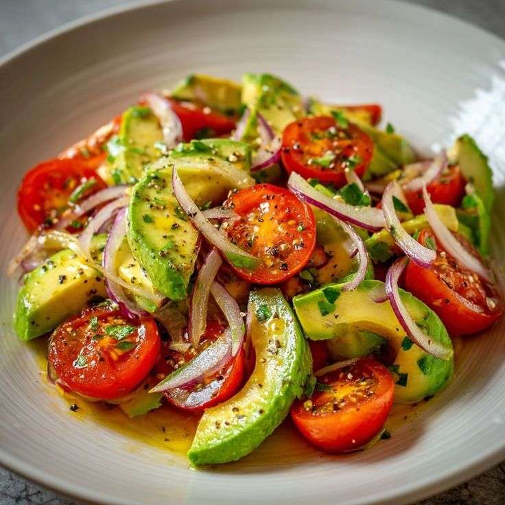 Salade fraîche avec avocat en cubes, tomates cerises coupées et fines lamelles d’oignon rouge, assaisonnée d’huile d’olive et citron.