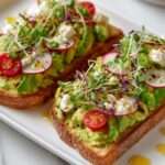 Tartines avocado toast garnies de feta émiettée, radis tranchés et tomates cerises sur pain grillé croustillant avec filet d’huile d’olive.