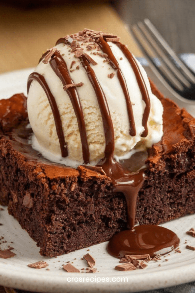 Brownie fondant au chocolat coupé en carrés, cœur moelleux et légèrement humide, servi avec glace vanille, sauce chocolat chaude et copeaux.