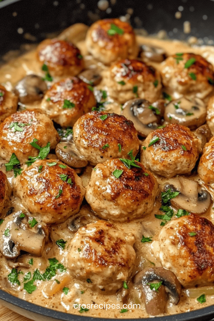 Boulettes de poulet dorées servies dans une sauce crémeuse aux champignons avec persil frais, accompagnées de pâtes ou de riz.