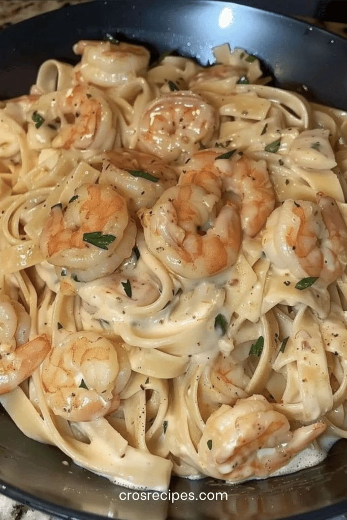 Assiette de pâtes crémeuses aux crevettes dorées, sauce onctueuse à l’ail et parmesan, garnie de persil frais.